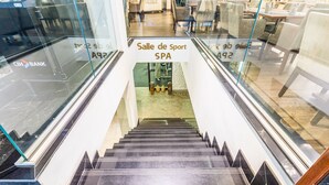 Una escalera interior que conduce a un área de 'Salle de Sport SPA' con barandillas de vidrio y un letrero de 'CIBANK' a la izquierda.