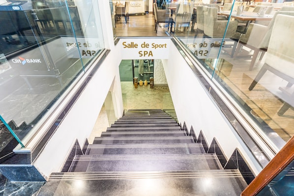Un escalier intérieur mène à un espace « salle de sport et spa », avec des rampes en verre et une enseigne « CIBANK » sur le côté gauche.
