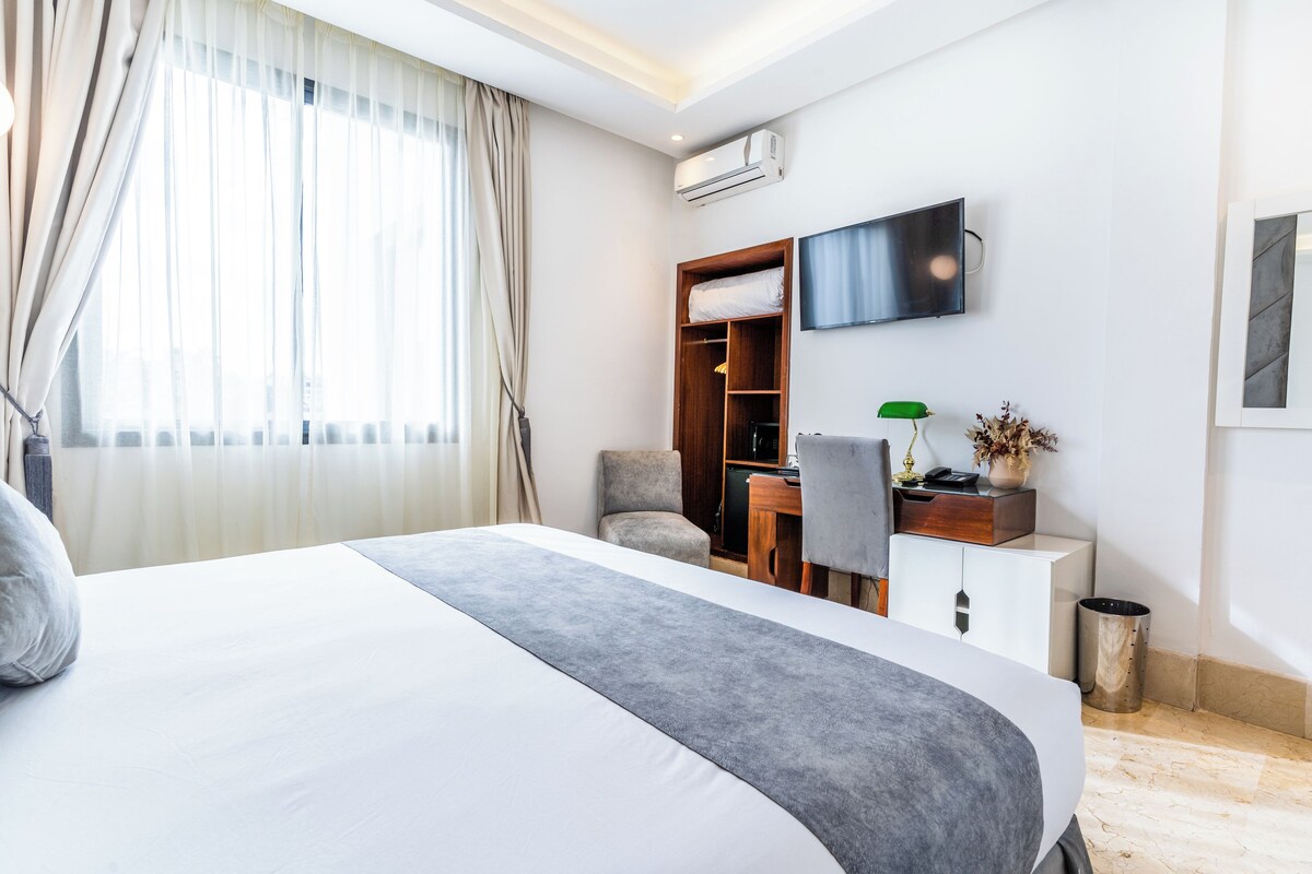 Hotelkamer met een groot bed, een bureau met stoel, een aan de muur bevestigde televisie en een raam met gordijnen.