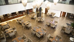 Un comedor amplio con varias mesas y sillas, una barra alargada con productos expuestos y una planta grande en el centro.
