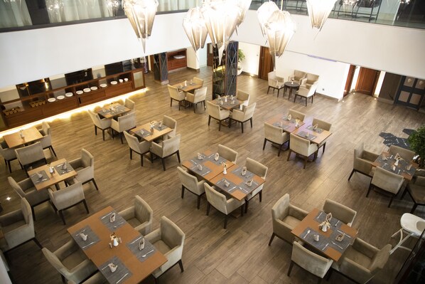 A spacious dining area with multiple tables and chairs, a long counter with a display of items, and a large plant in the center. - One hotel Casablanca (Casablanca)