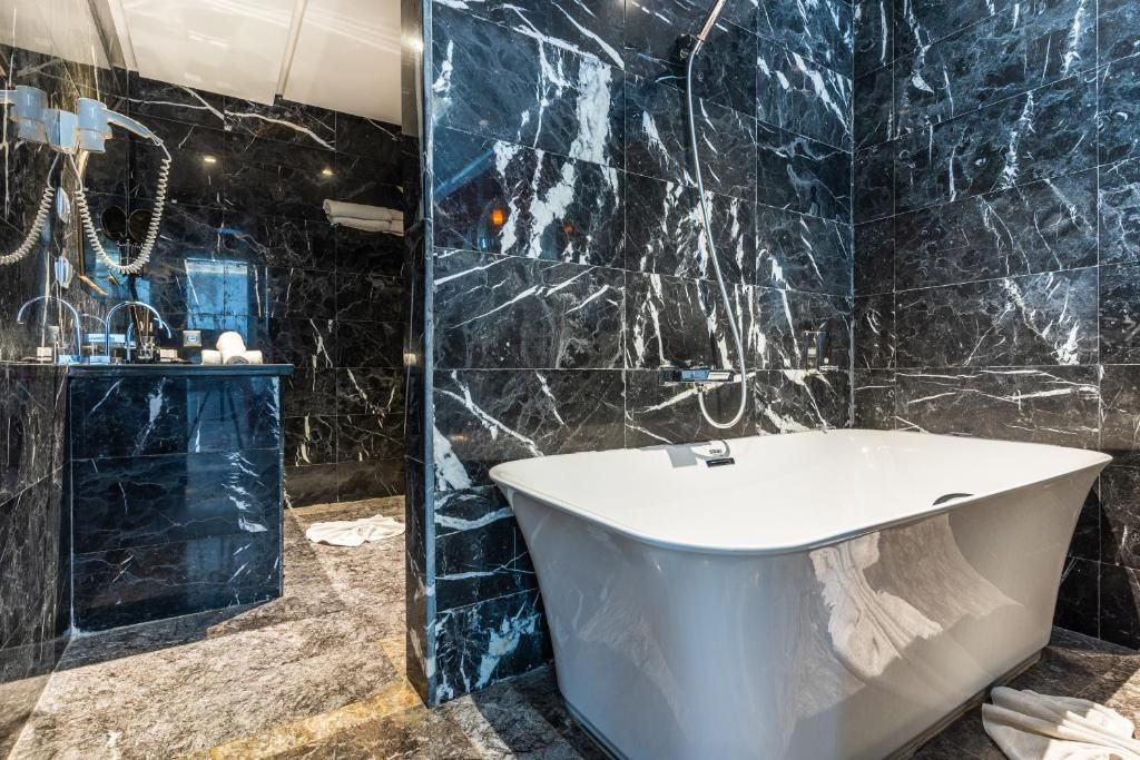 A modern bathroom with a freestanding bathtub, marble walls, and a glass-enclosed shower area.