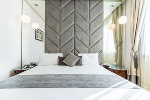 Une chambre d’hôtel moderne avec un grand lit, une tête de lit aux motifs géométriques, des tables de chevet et des luminaires suspendus.