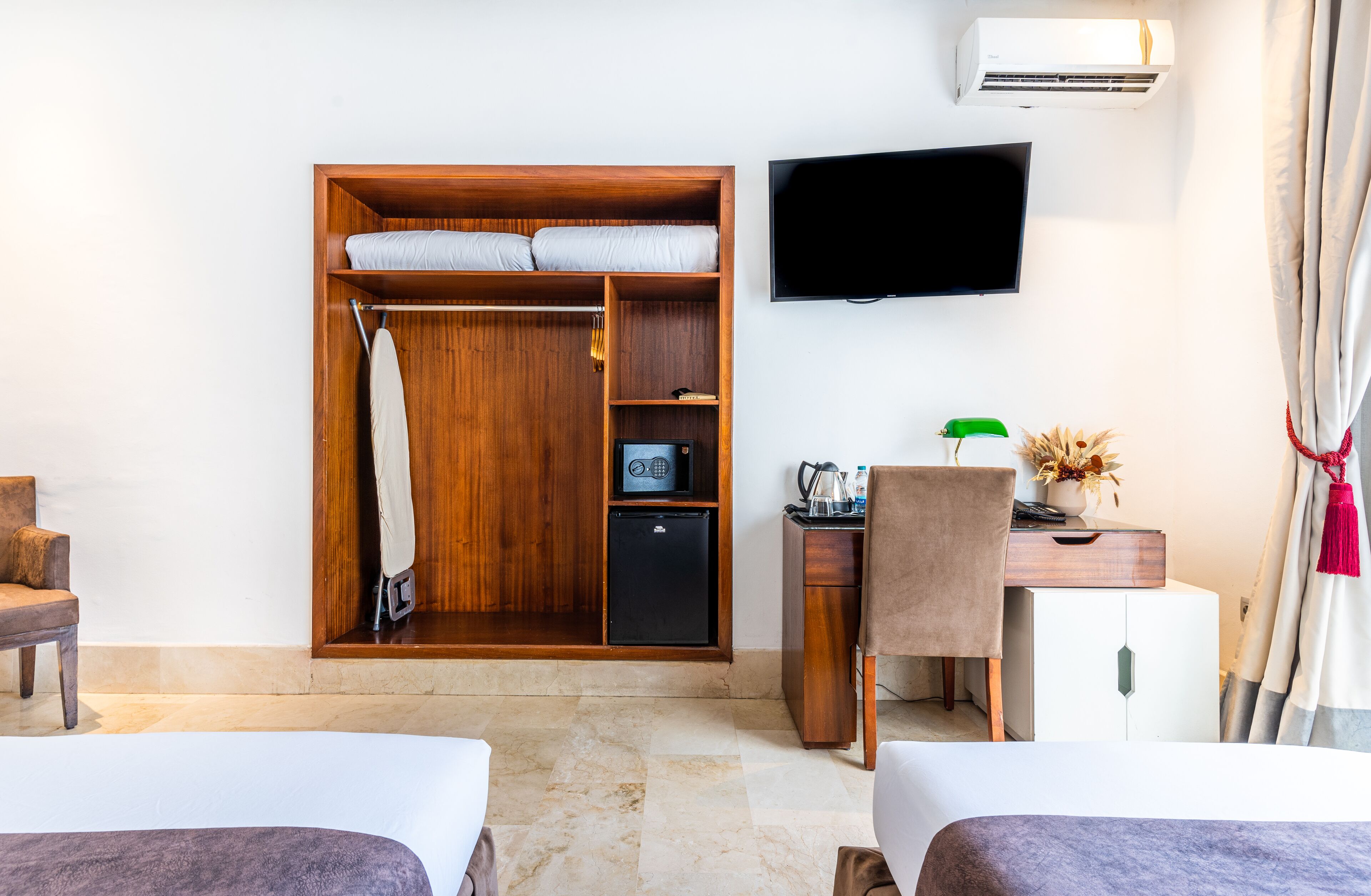 A hotel room with a wooden wardrobe, a desk with a chair, a television mounted on the wall, and a bed.