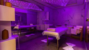 A modern spa room with a purple-lit ceiling, marble walls, and multiple treatment tables.
