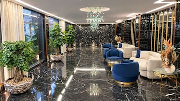 Un vestíbulo moderno con piso de mármol, asientos azul y blanco, y plantas decorativas.