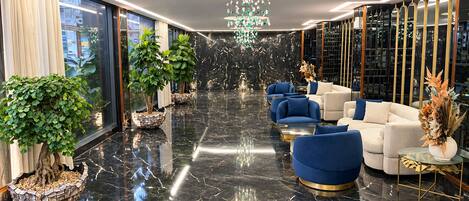 Un vestíbulo moderno con piso de mármol, asientos azul y blanco, y plantas decorativas.