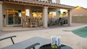 Een overdekt terrasgedeelte met tuinmeubilair, een zwembad en Corona biervaten op een tafel.