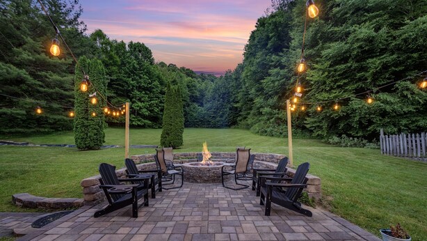 A patio with outdoor seating and a fire pit, surrounded by trees and a wooden fence.