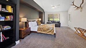 A bedroom with a bed, nightstands, a bookshelf, a gray sofa, and a deer antler on the wall.