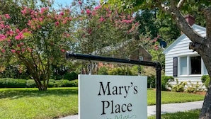 Une enseigne indiquant « Chez Mary », dans un quartier résidentiel, avec une pelouse bien entretenue et des arbres en fleurs.