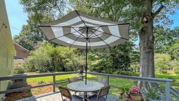Une terrasse en bois avec une table ronde et des chaises, un grand parasol et des plantes en pot.