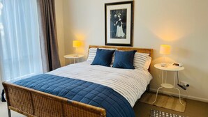 Een hotelkamer met een bed, twee nachtkastjes met lampen, een lijst aan de muur en een raam met gordijnen.