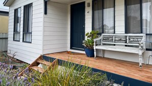 Een wit huis met een donkerblauwe deur, een bankje en een bloempot op de veranda.