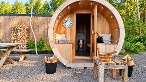 A wooden barrel-shaped structure with a fireplace, a clock, and a cat inside.