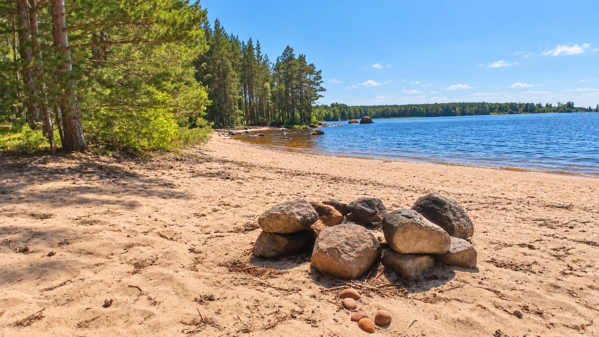 Hiekkainen ranta, jonka edessä on kivikasa ja taustalla tyyni järvi.