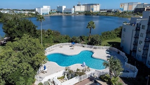 A swimming pool with a curved design, surrounded by a white fence, and located near a body of water with buildings in the background. - The Enclave Hotel and Suites (Orlando)