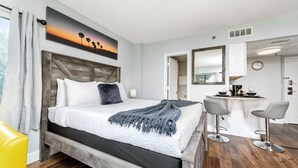 A hotel room with a bed, a desk with two chairs, a painting on the wall, and a clock. - The Enclave Hotel and Suites (Orlando)