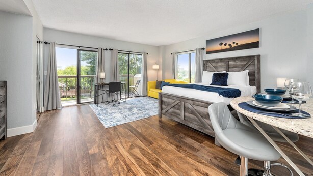 A modern bedroom with a bed, a dining table, and a view of the outdoors. - The Enclave Hotel and Suites (Orlando)