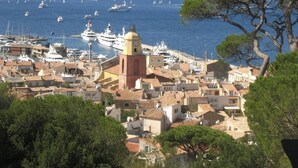 Une ville côtière dotée d’une tour imposante, d’un port de plaisance avec des bateaux, et dont le paysage est dominé par des collines.