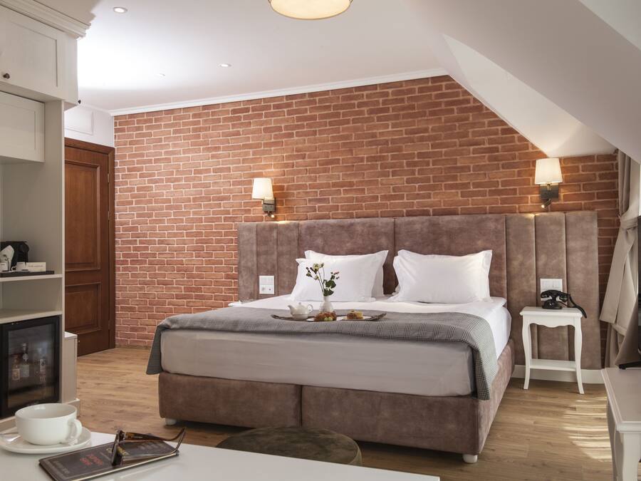 A modern hotel room with a brick wall, a large bed with a headboard, bedside tables, a desk, and a television.