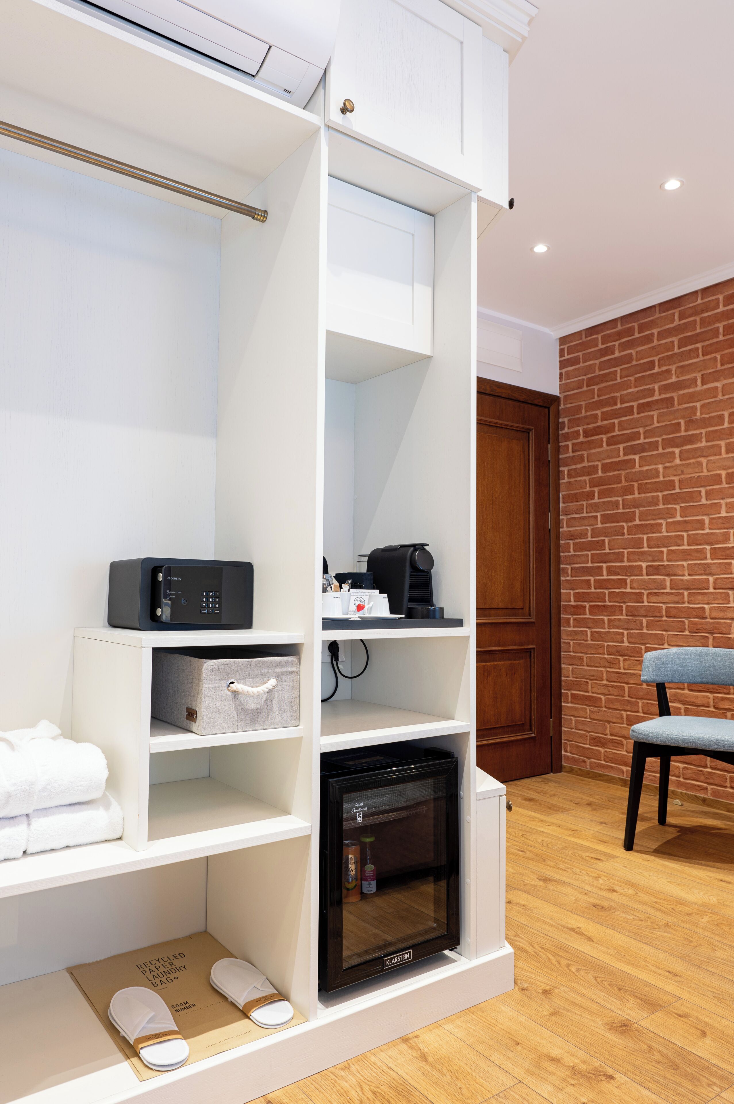 A compact hotel room with a built-in wardrobe, a microwave, a coffee machine, and a small seating area.