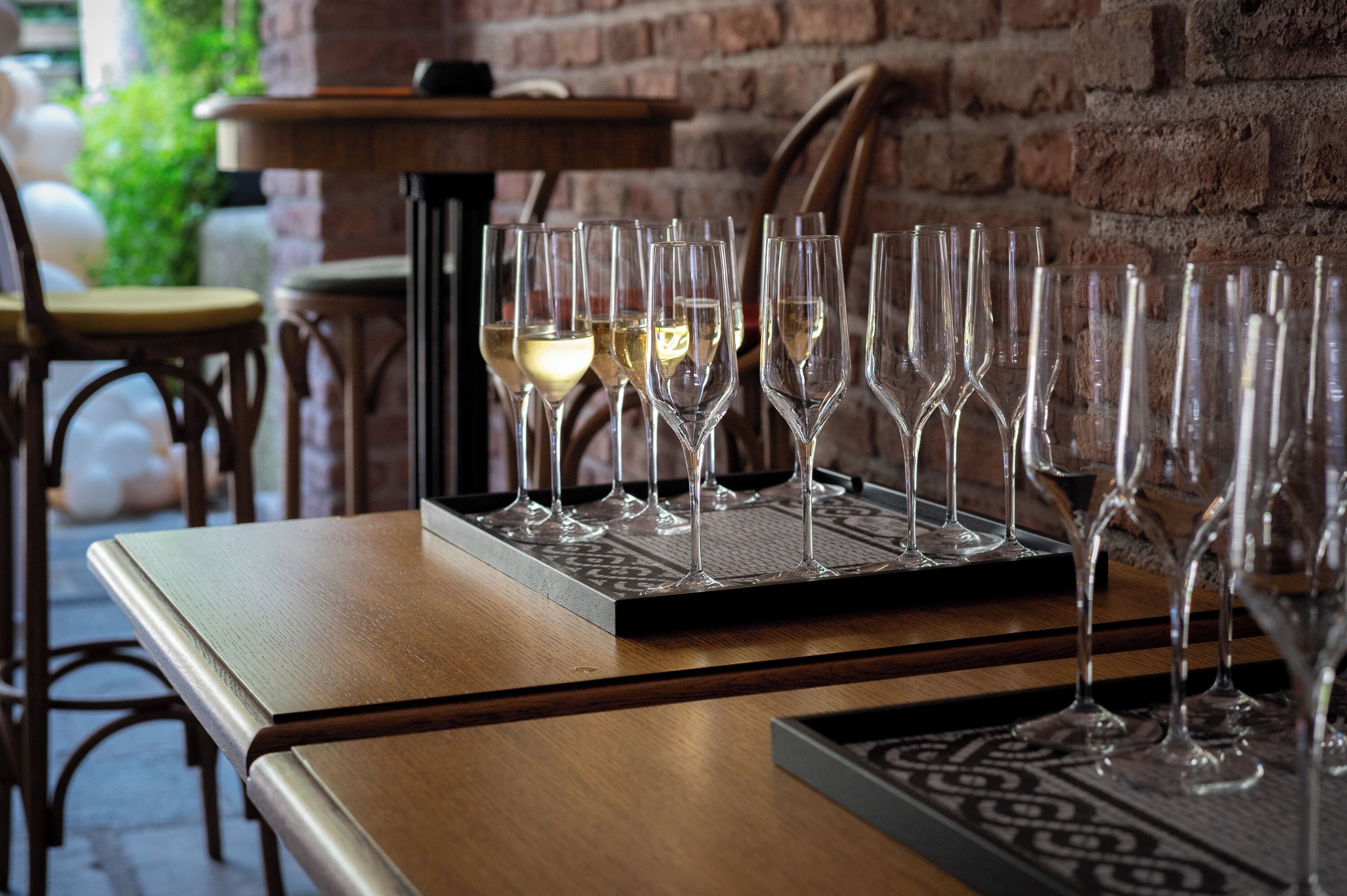Ein Tisch mit mehreren Weingläsern, einige gefüllt mit einer klaren Flüssigkeit, wahrscheinlich Wein, und einem Tablett mit weiteren Gläsern.