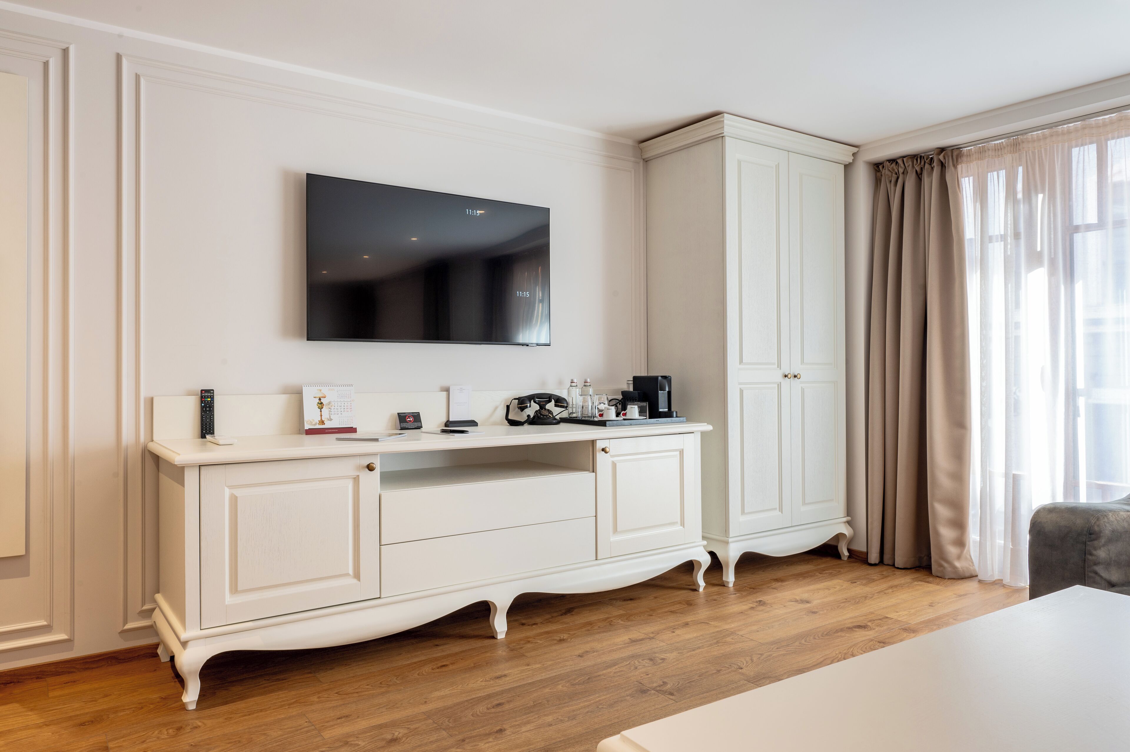 Una habitación de hotel moderna con una mesa blanca, un televisor de pantalla plana, un armario y una ventana con cortinas.