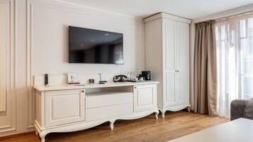Una habitación de hotel moderna con una mesa blanca, un televisor de pantalla plana, un armario y una ventana con cortinas.
