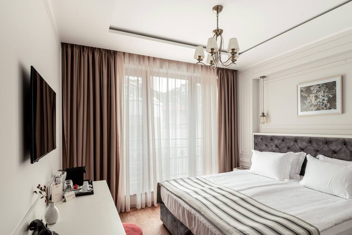 Ein Hotelzimmer mit einem Bett, einem Schreibtisch mit Lampe, einem Fernseher und einer Kristallleuchter.