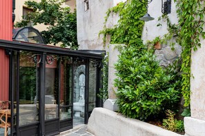 Un espace extérieur aménagé avec des sièges, protégé par des parois de verre, et agrémenté d’un mur en pierre et de verdure.