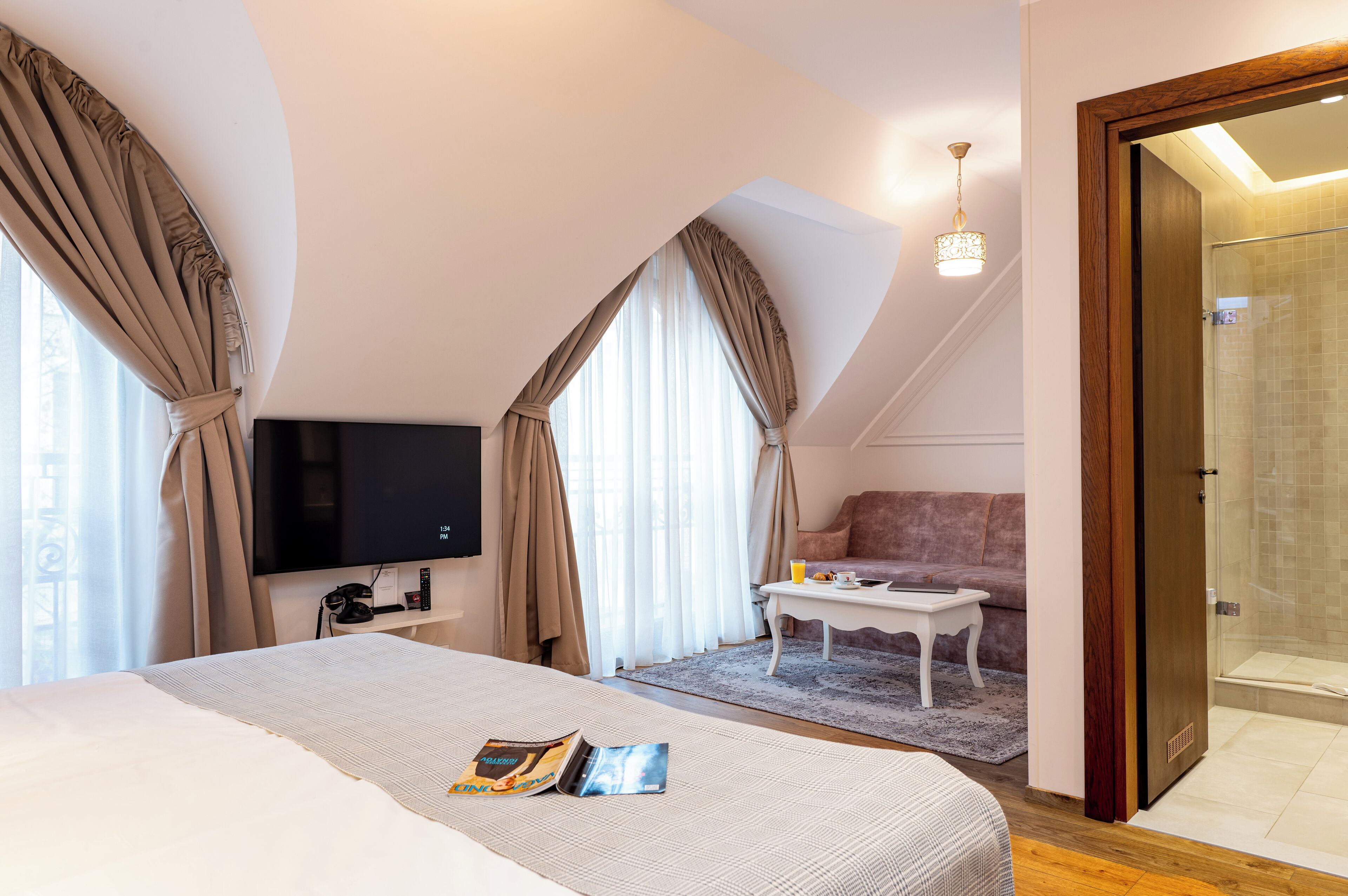 A modern hotel room with a large bed, a TV, a sofa, a coffee table, and a shower area.