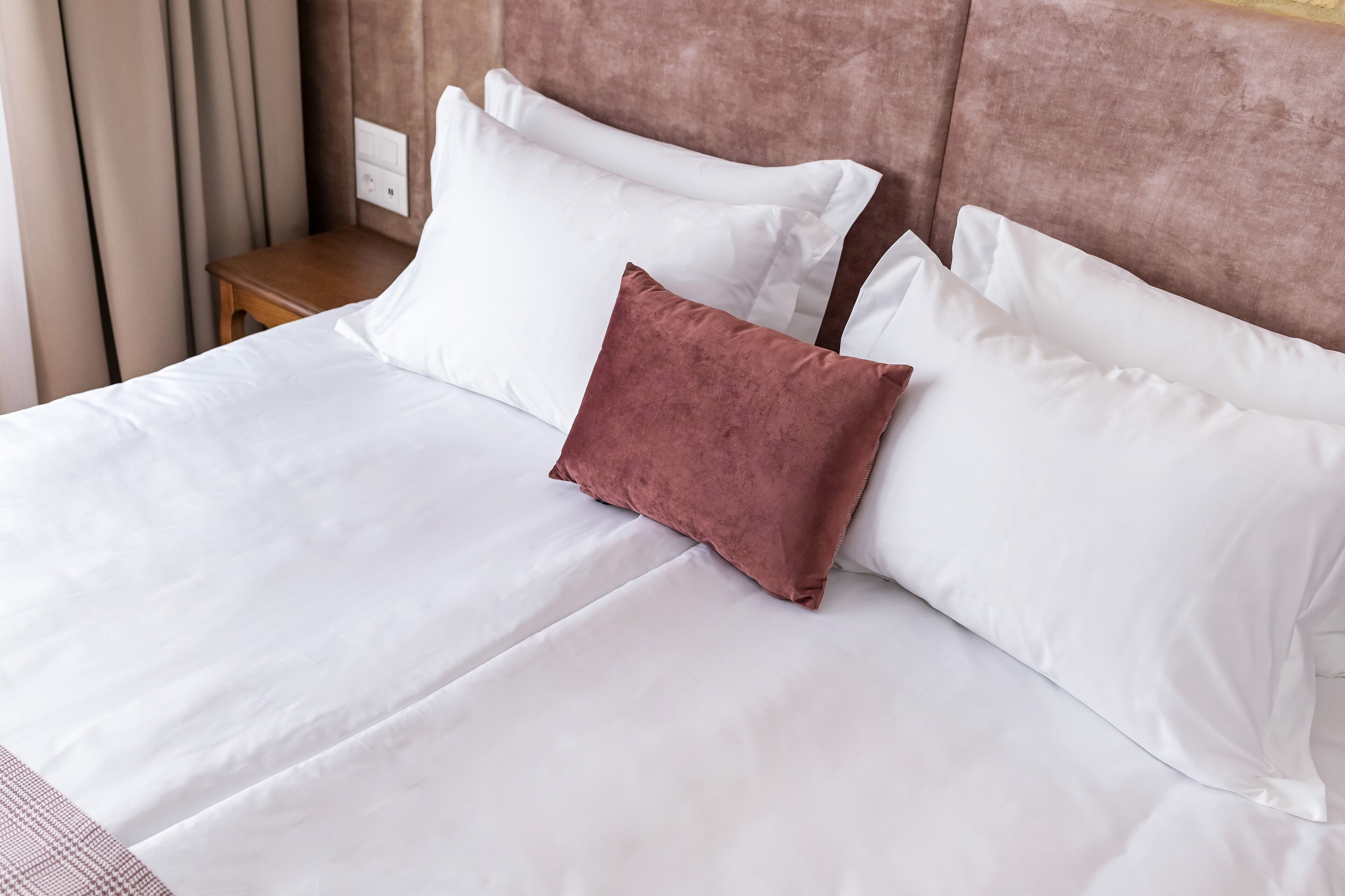 Una cama bien hecha con sábanas blancas y una almohada marrón.