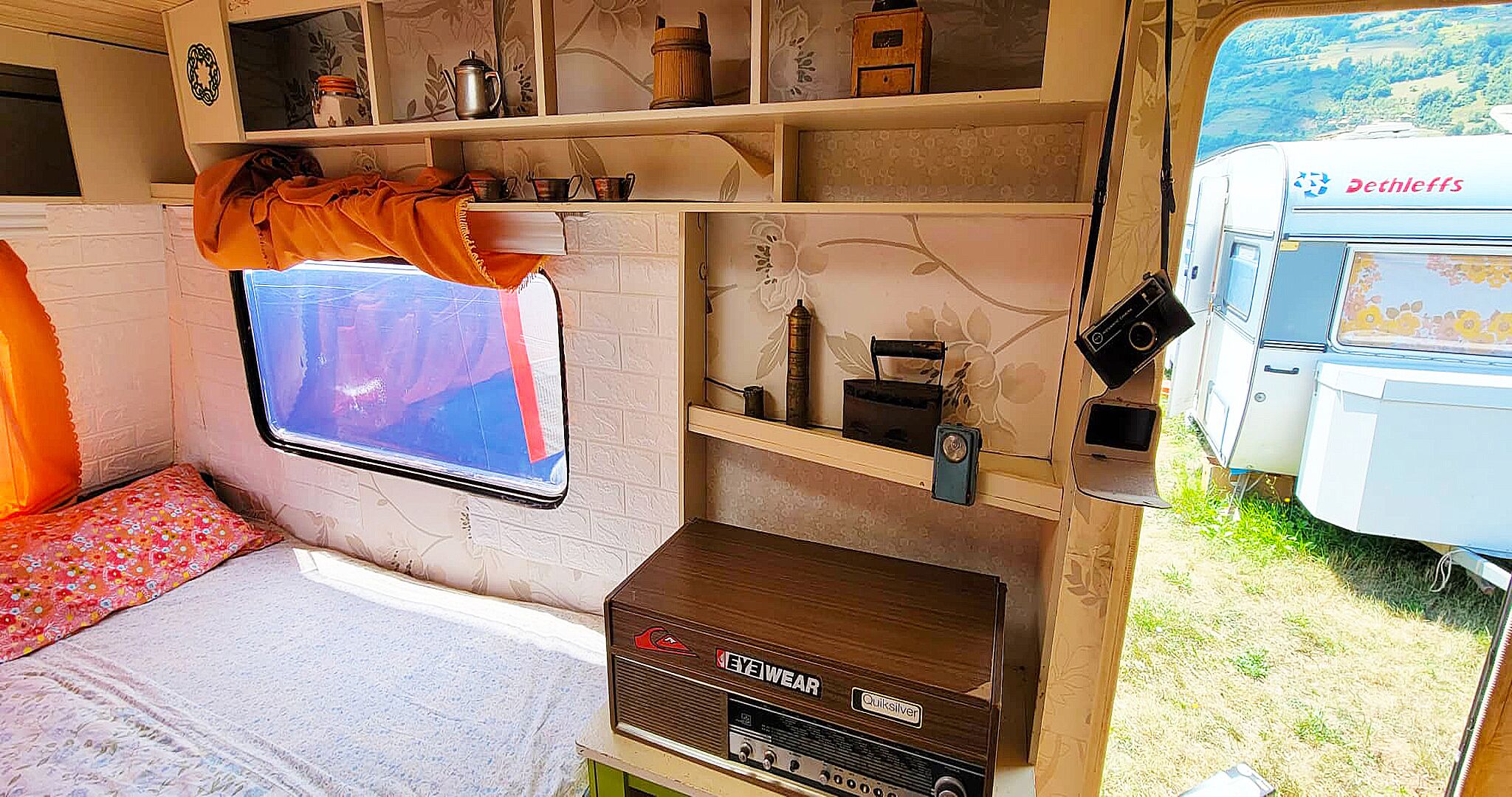 Interior compacto de una caravana con cama, ventana y una pequeña cocina.
