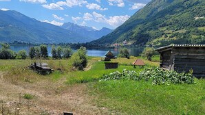 A rural landscape with a lake, mountains, and a wooden cabin.
