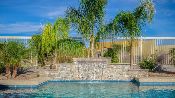 A swimming pool with a stone wall and palm trees, surrounded by a fence. - Like New Home Private pool ,New furnishings, 20 mins to State Farm stadium  (Buckeye)