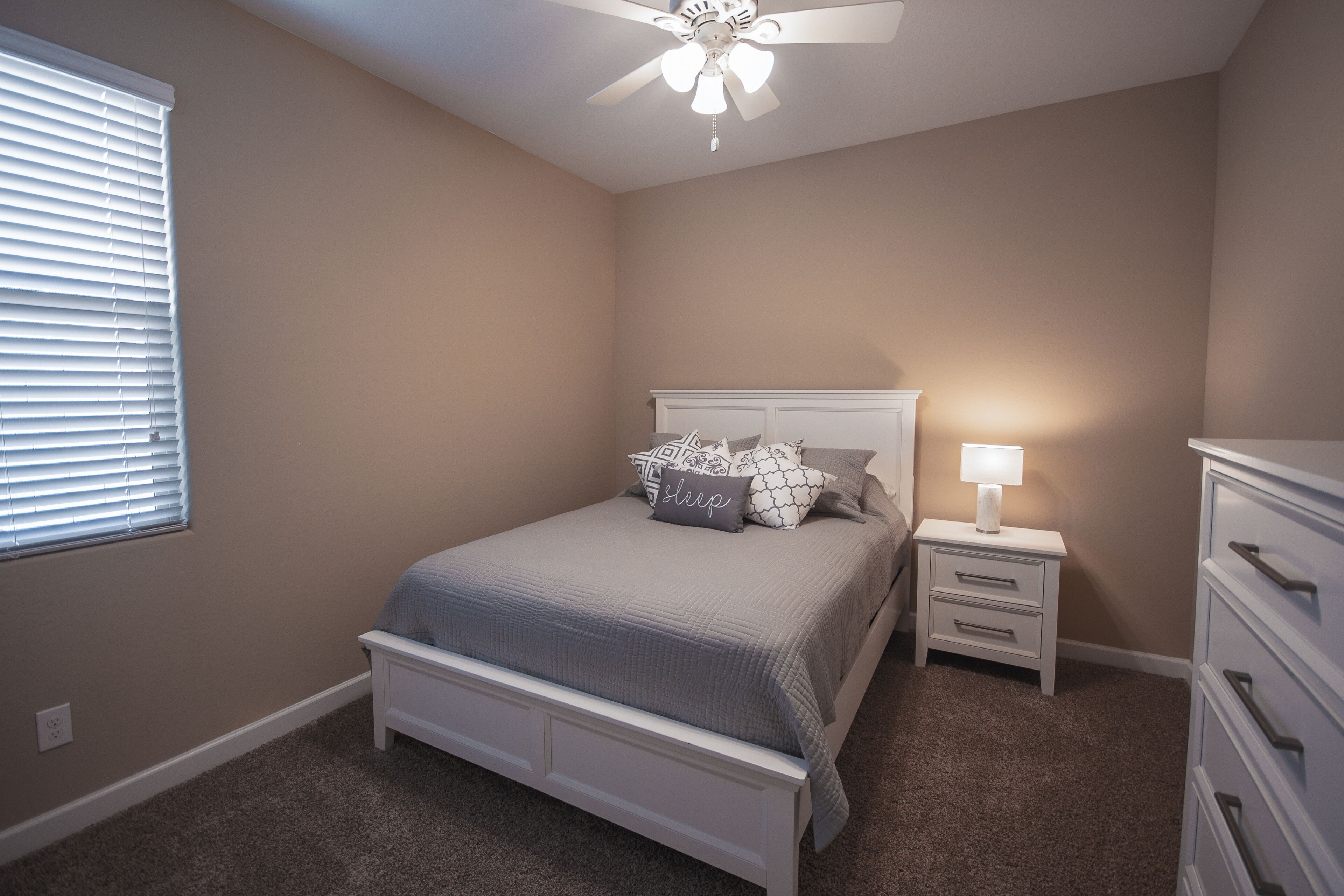 Un dormitorio con cama, mesita de noche, cómoda y ventilador de techo.