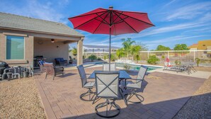 A patio with a table and chairs, a red umbrella, and a pool in the background. - Like New Home Private pool ,New furnishings, 20 mins to State Farm stadium  (Buckeye)