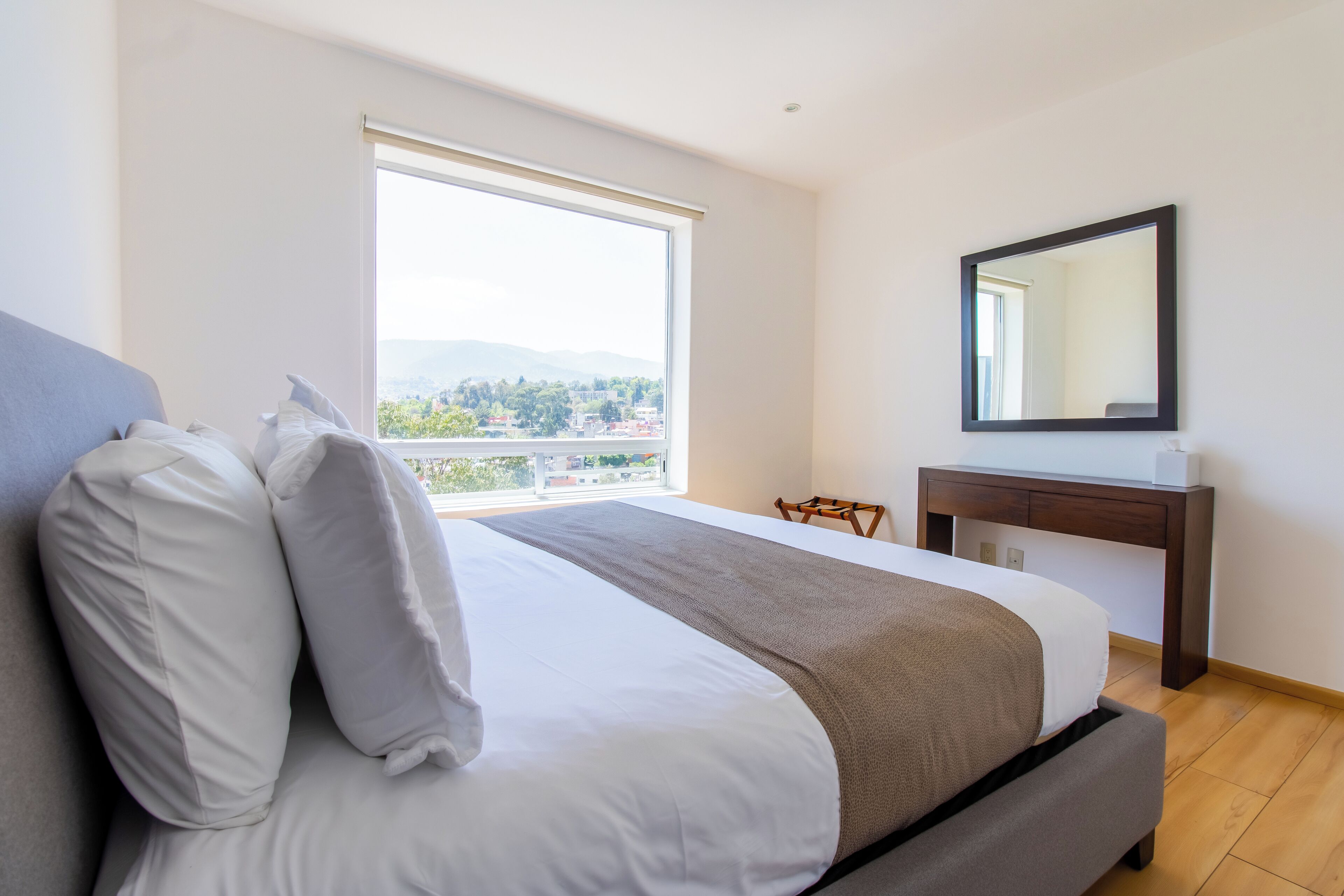 A hotel room with a large bed, a desk, and a window with a city view.
