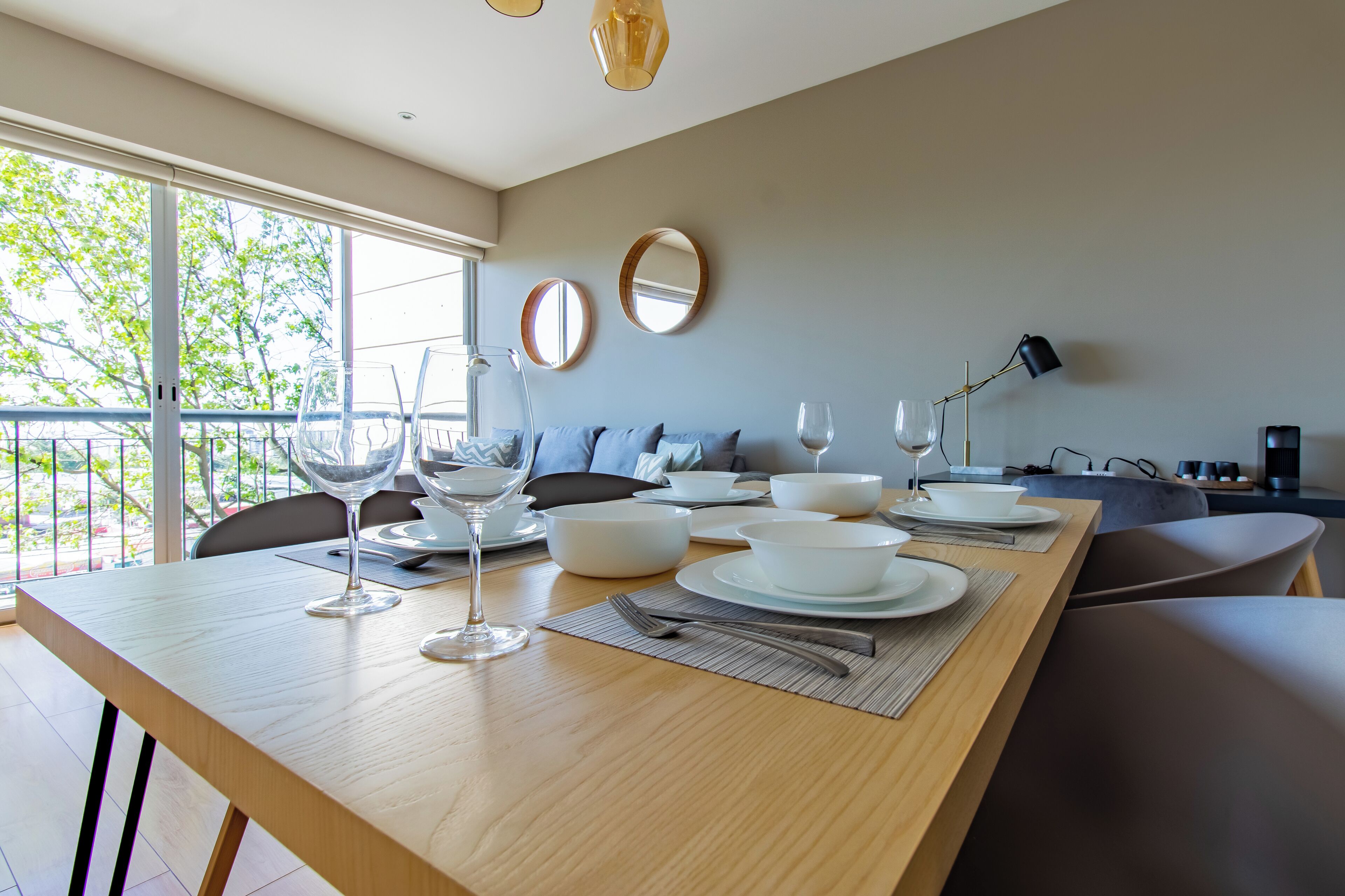 A modern dining area with a wooden table set for a meal, a sofa, and a balcony view.