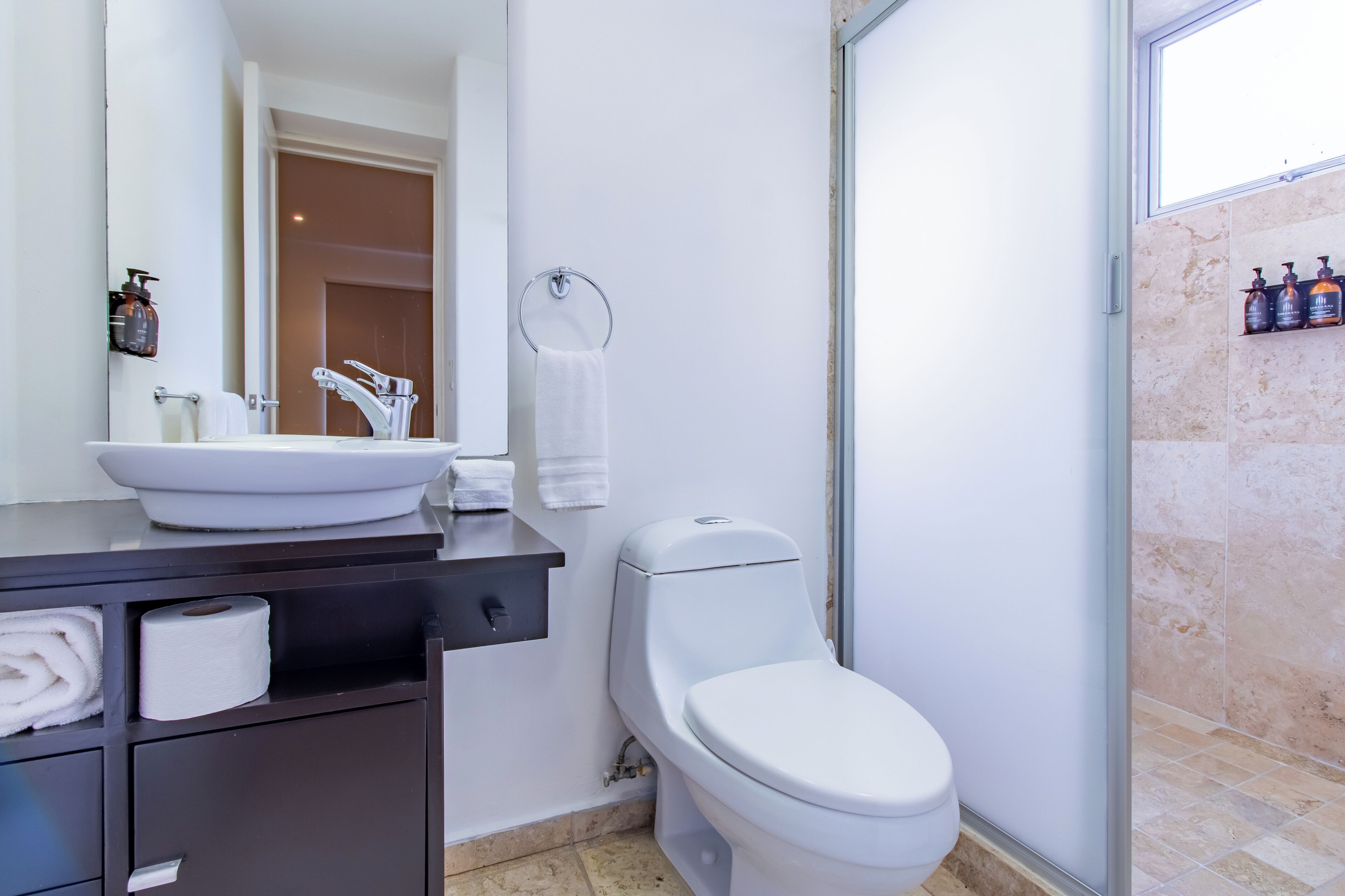 A modern bathroom with a white sink, toilet, and shower. There are towels and toiletries on the counter.