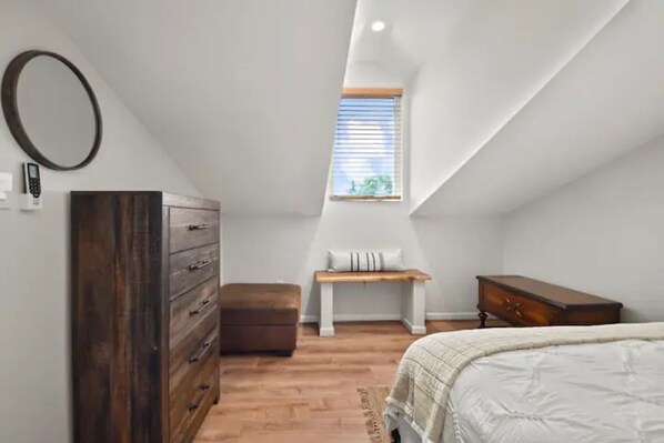 A bedroom with a sloped ceiling, a wooden dresser, a bench, and a bed.