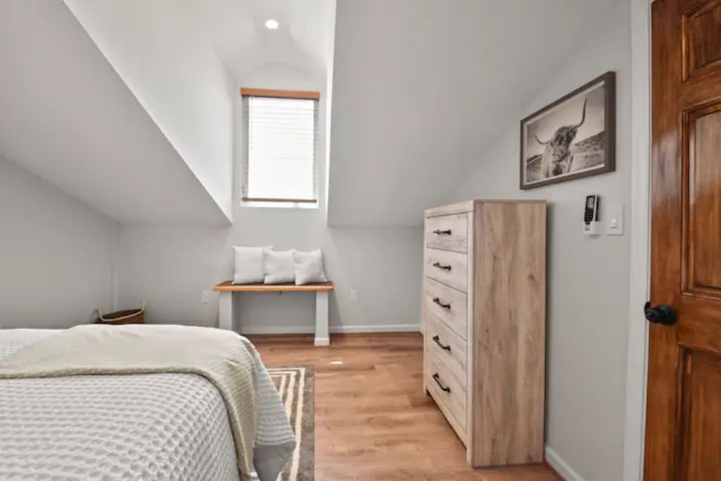 Une chambre à coucher avec un lit, une commode en bois, un banc et une fenêtre.