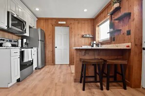A kitchen with white cabinets, a microwave, a refrigerator, and wooden flooring.
