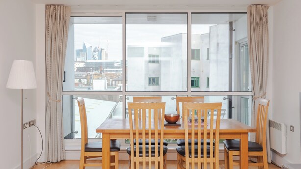 Un coin repas comprenant une table et des chaises, une lampe, et une vue sur le paysage urbain grâce à de grandes fenêtres.