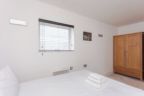 Quarto com cama, janela com persianas, guarda-roupa de madeira e um pequeno quadro na parede.