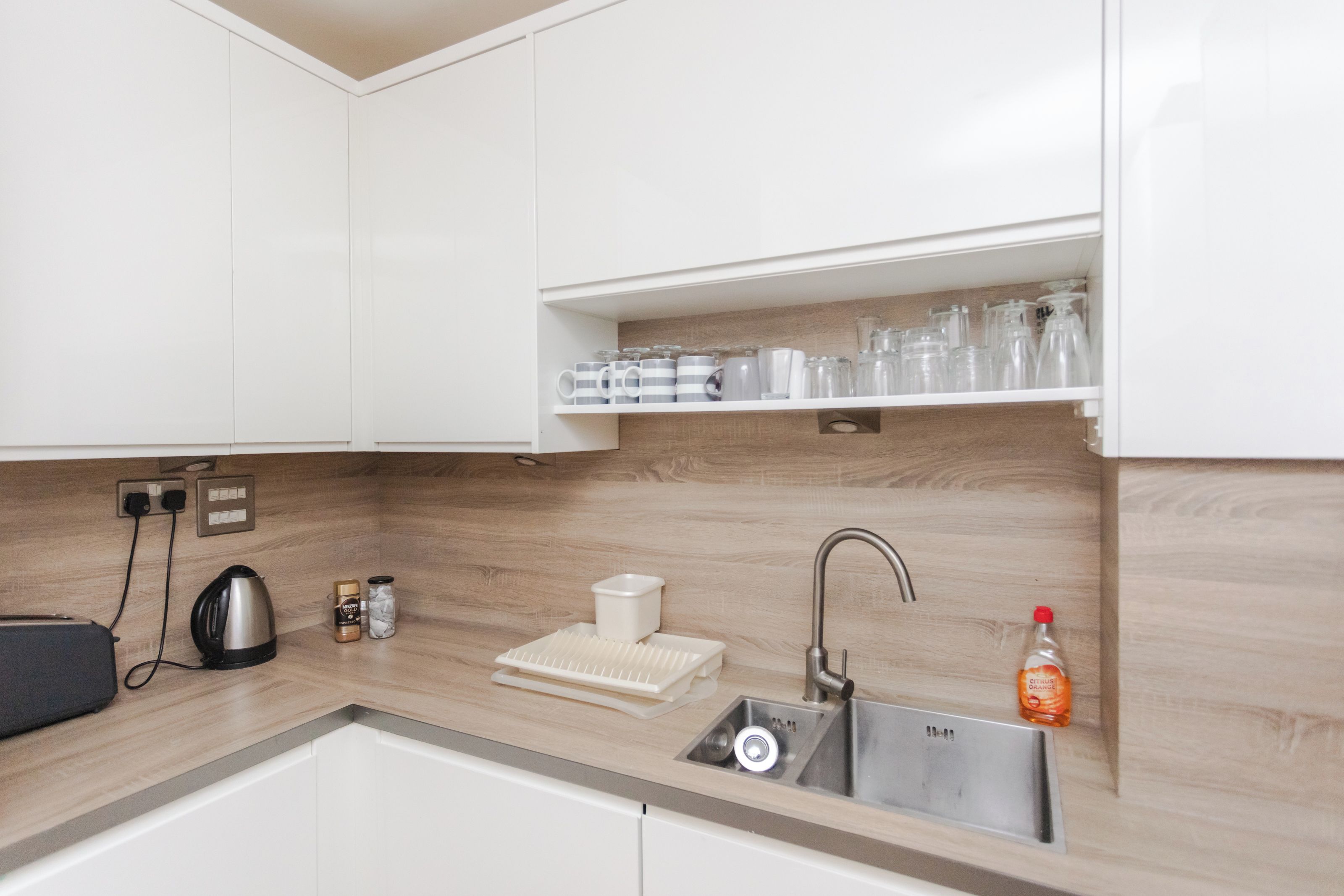 A modern kitchen with white cabinets, a wooden backsplash, a stainless steel sink, and a coffee machine.