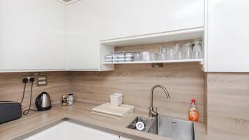 A modern kitchen with white cabinets, a wooden backsplash, a stainless steel sink, and a coffee machine.