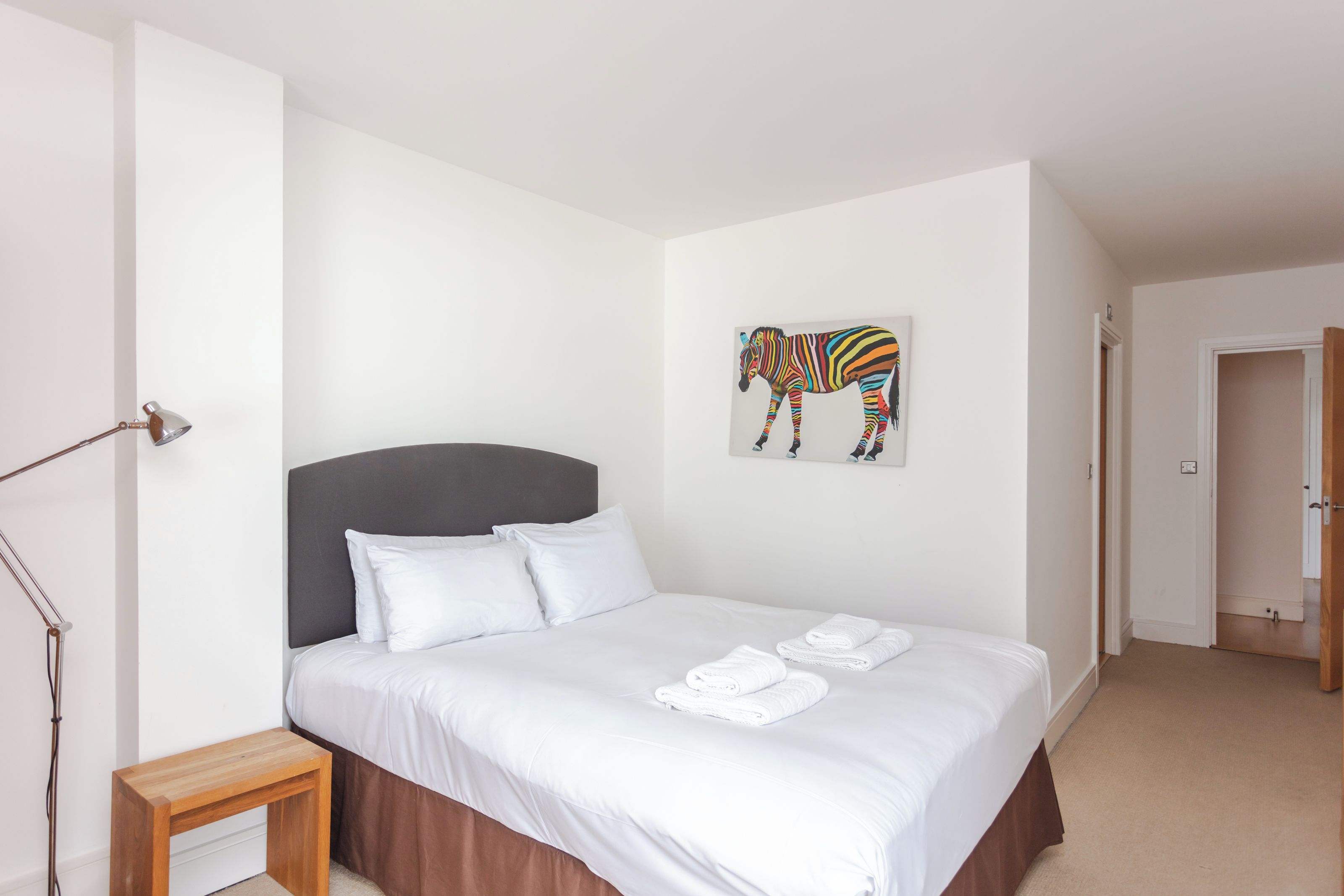 Une chambre à coucher avec un lit, une table de chevet, une lampe et un tableau représentant une zèbre accroché au mur.