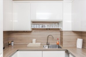 Une cuisine moderne avec des meubles blancs, un évier en acier inoxydable et un plan de travail en bois.